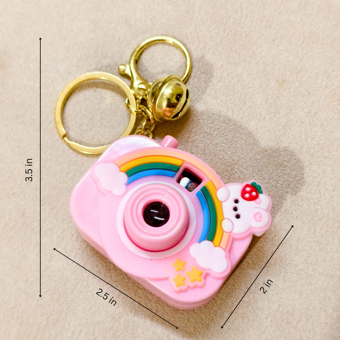 Pink camera-shaped keychain with rainbow design and measurements on a beige background