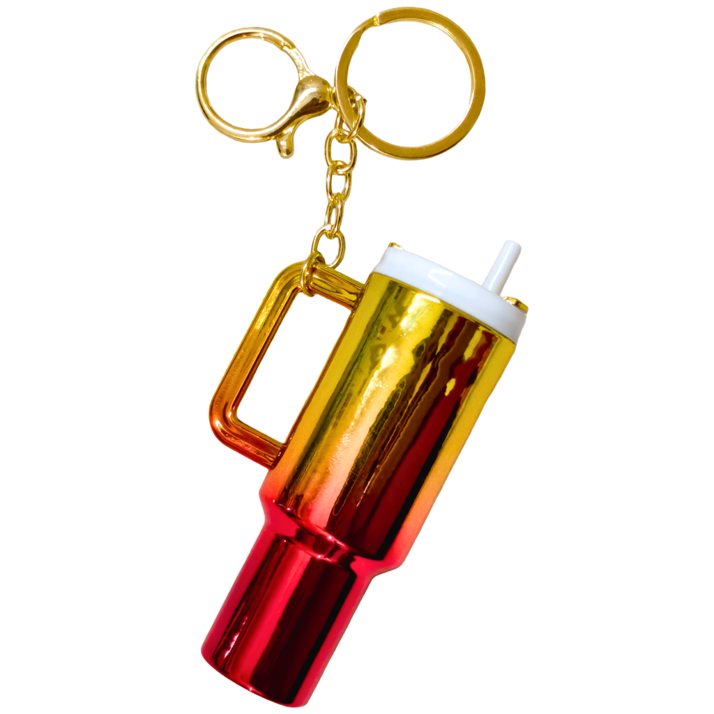 A metallic keychain shaped like a handled tumbler, featuring a gold-to-red gradient body, a white lid with a straw, and gold key rings on a plain white background.