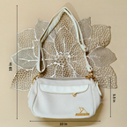 White handbag with gold accents on a beige background with leaf patterns