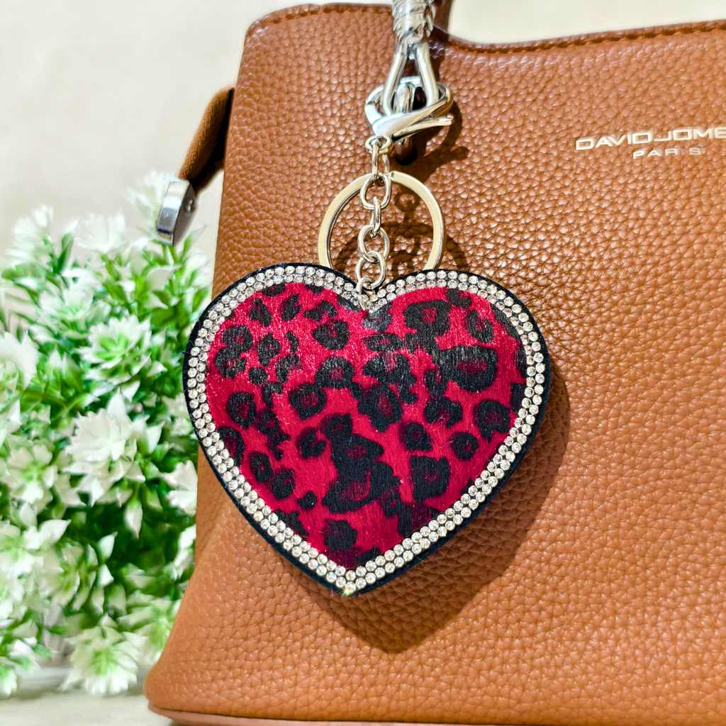 Red Leopard Heart Bag Charm Attached On Purse In The Front Of Beige Background. 
