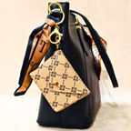Black handbag with a gold tag and ribbon on a beige background