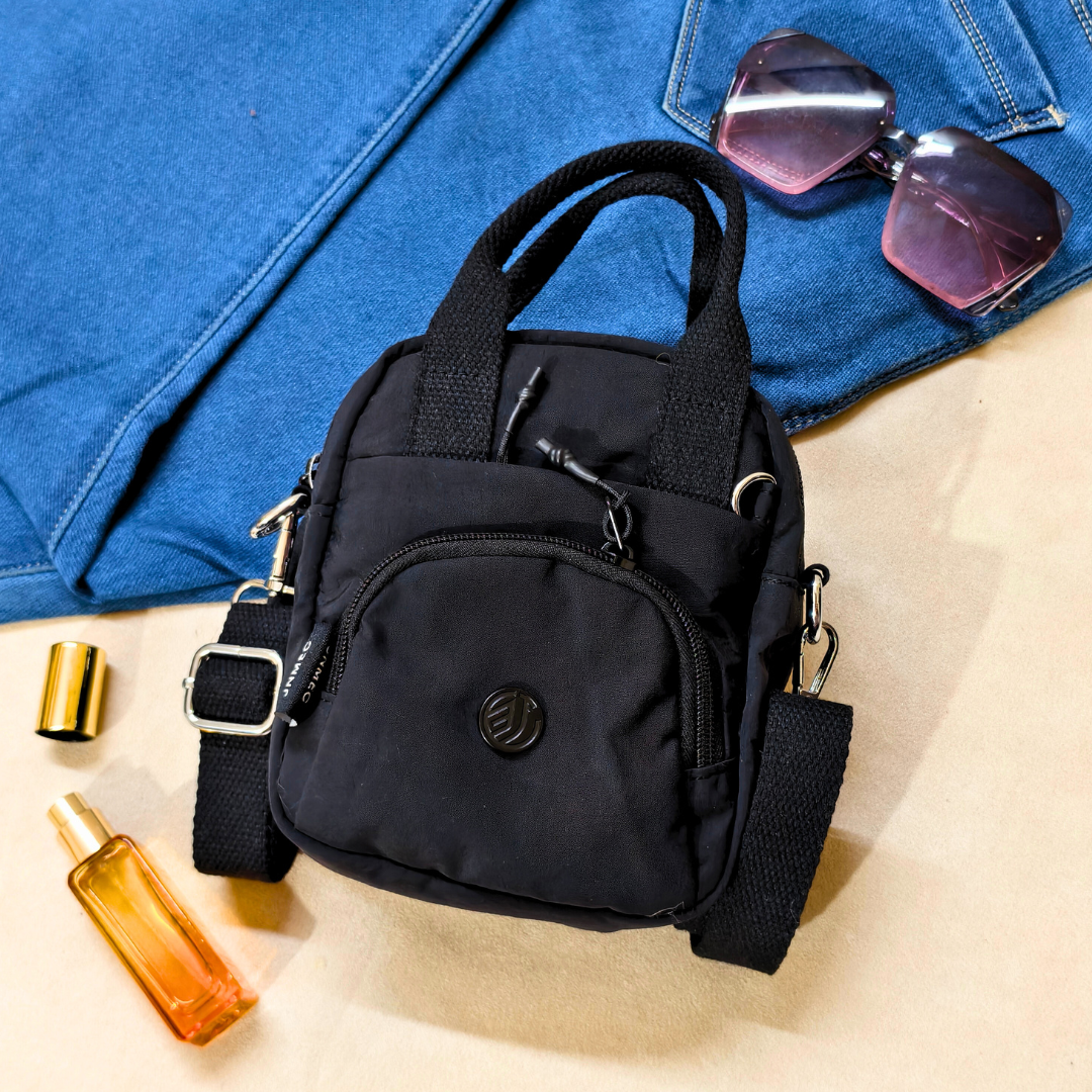 Black backpack on a blue denim surface with sunglasses and a bottle nearby