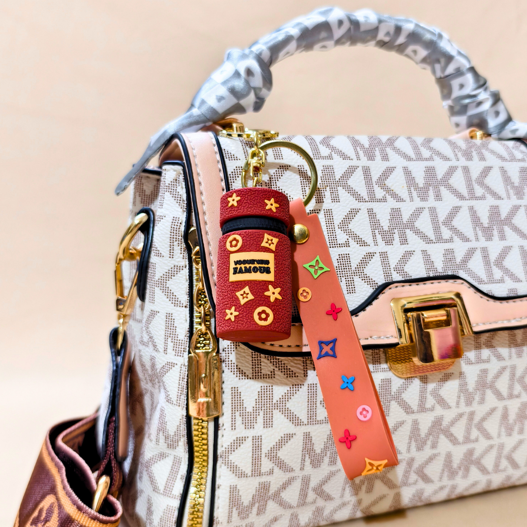 Brown cylinder keychain on a white printed purse in front of a beige background.