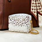 White pouch with leopard print and gold keychain in front of a brown leather bag.