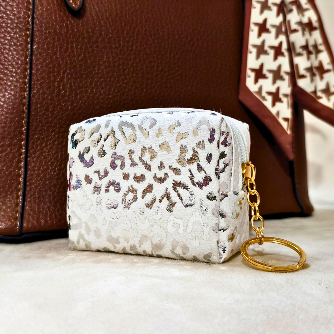 White pouch with leopard print and gold keychain in front of a brown leather bag.