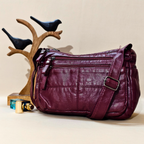 Purple leather handbag on a beige surface with decorative elements.