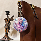 Colorful fairy-themed keychain attached to a brown leather bag with a statue in the background.