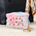 Pink and white quilted pouch with embellishments and a keychain, placed on a surface.