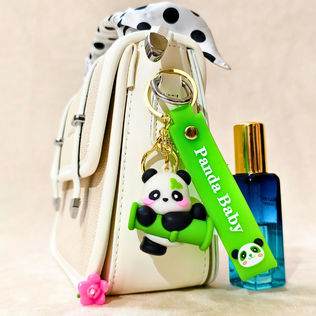 Panda keychain with a green tag labeled 'Panda Baby' attached to a white bag, next to a blue perfume bottle.