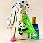 Panda keychain with a green tag labeled 'Panda Baby' attached to a white bag, next to a blue perfume bottle.
