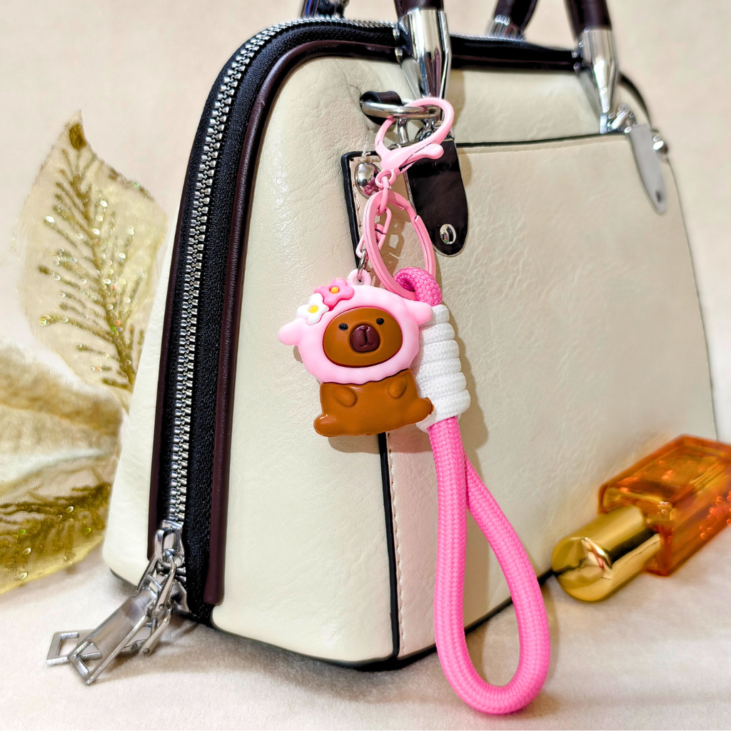 Pink keychain with a bear design attached to a beige handbag.