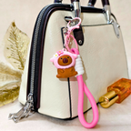 Pink keychain with a bear design attached to a beige handbag.