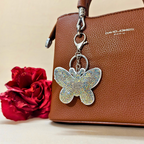 white butterfly with metal latch placed on a purse beside a red flower in front of a beige background