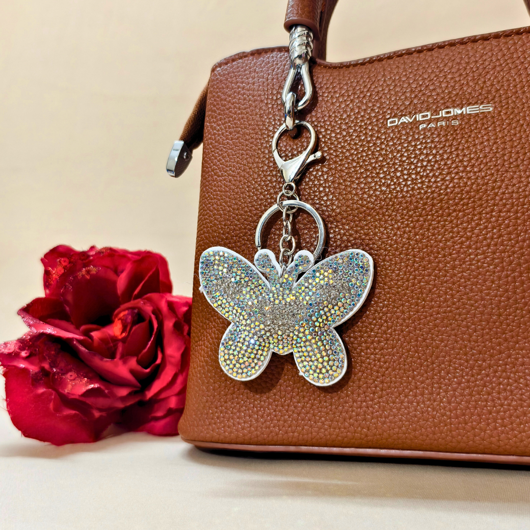 white butterfly with metal latch placed on a purse beside a red flower in front of a beige background