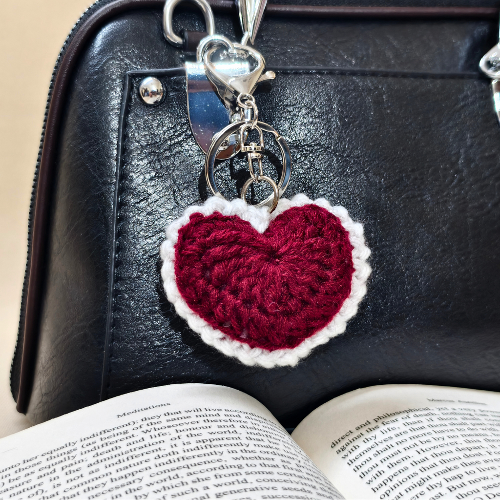 Heart-shaped keychain on a black leather bag with an open book underneath