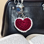 Heart-shaped keychain on a black leather bag with an open book underneath