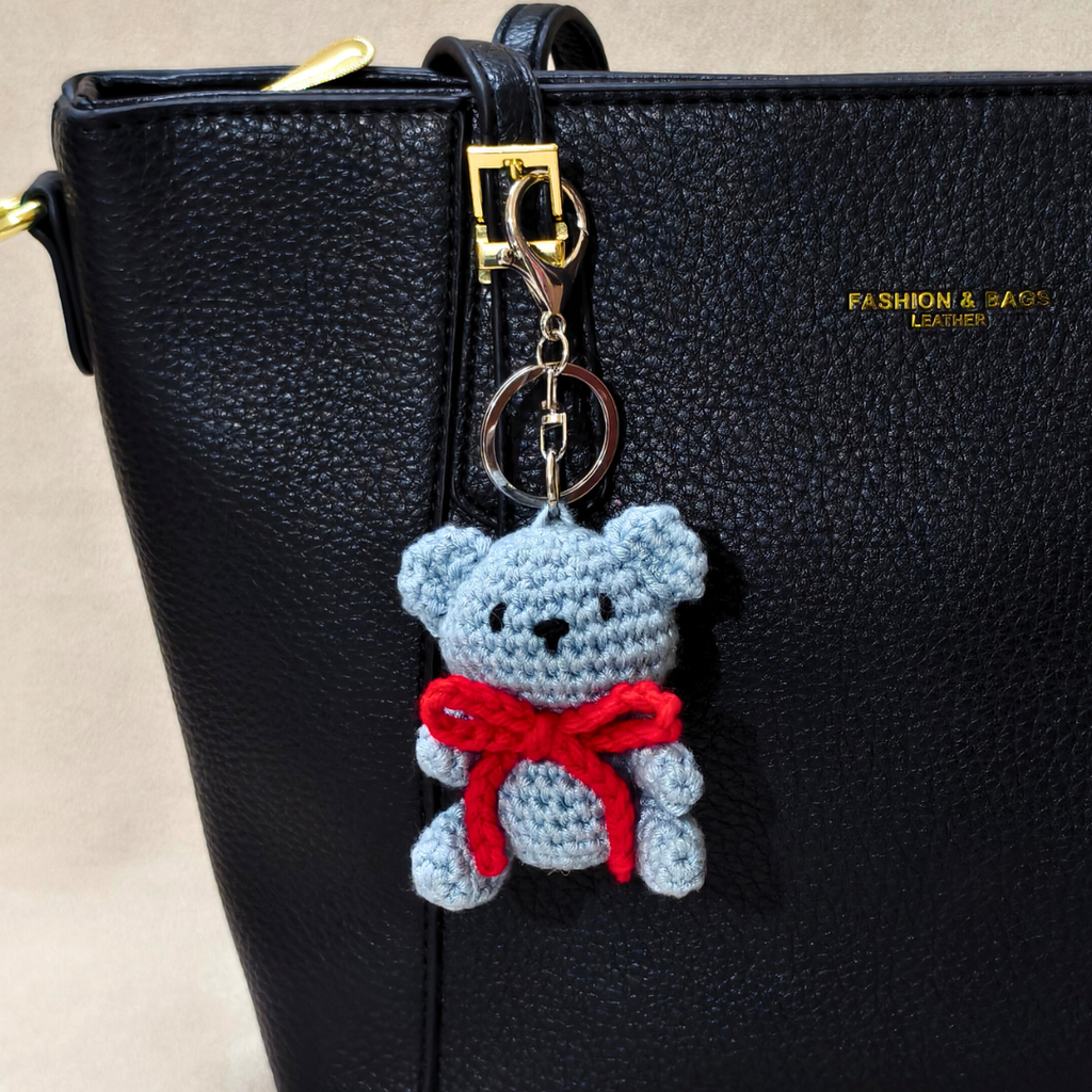 Crocheted bear keychain with a red bow attached to a black handbag.