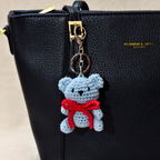 Crocheted bear keychain with a red bow attached to a black handbag.