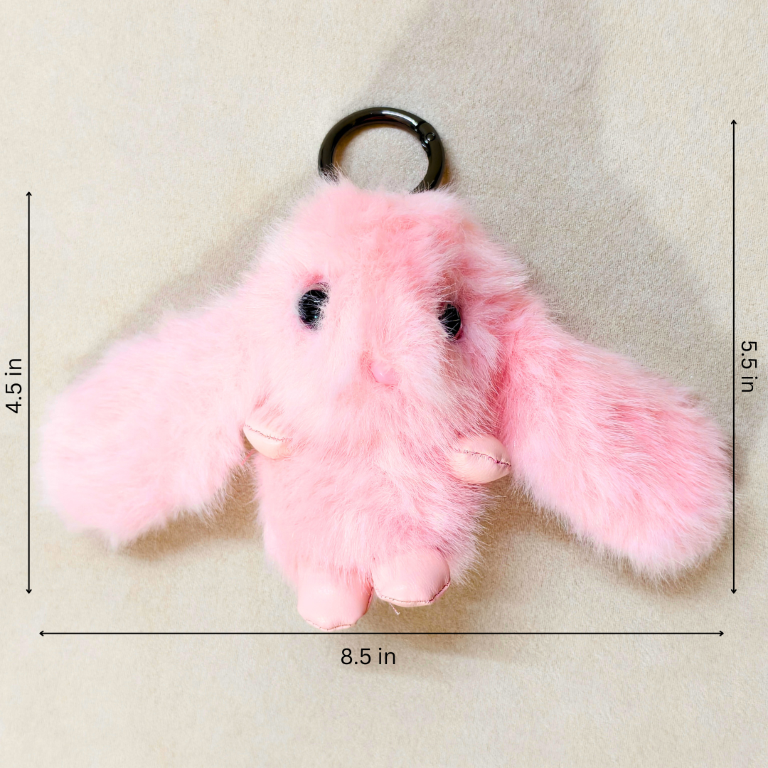 A pink fluffy bunny keychain with long floppy ears, black bead eyes, small pink feet, and a black metal key ring, shown on a light beige background with measurement lines and labels indicating 4.5 in height, 5.