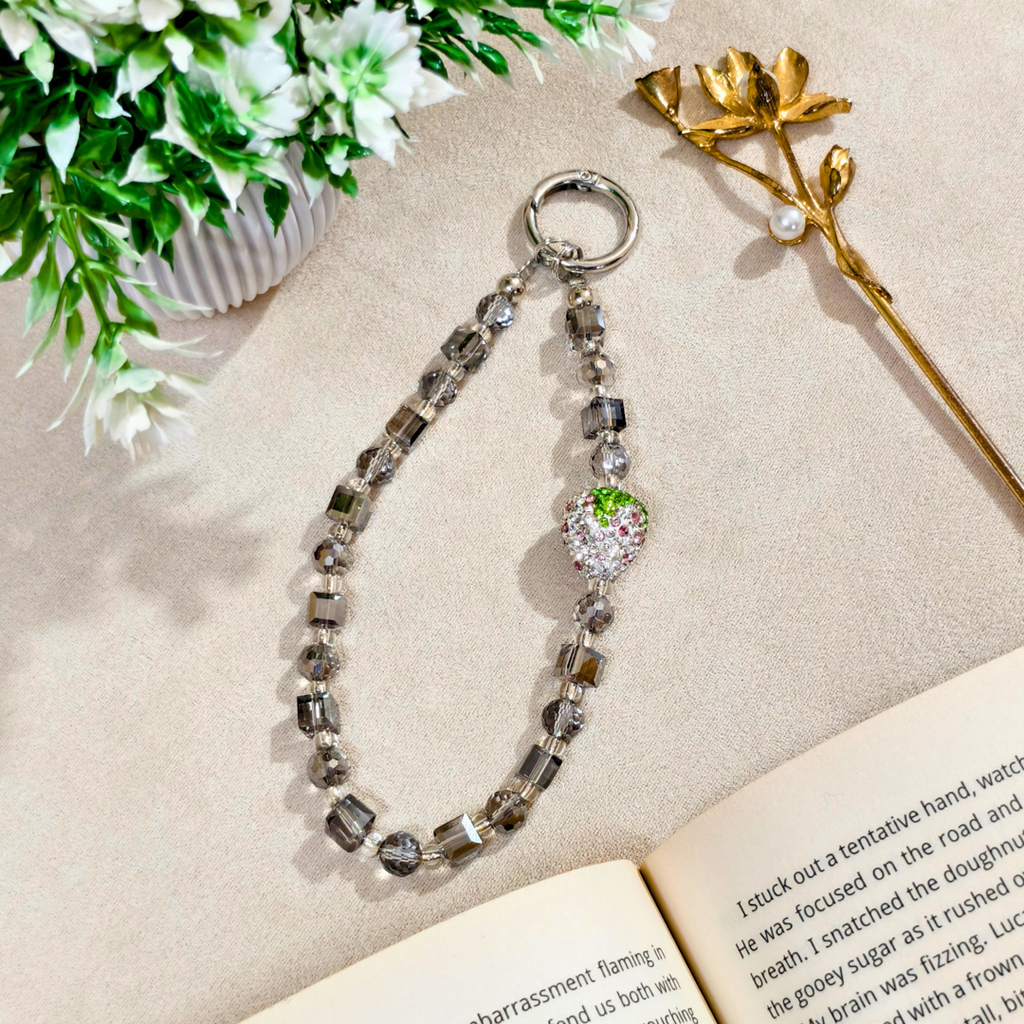 Decorative keychain with beads and a heart-shaped charm on an open book with flowers and a gold pen in the background.