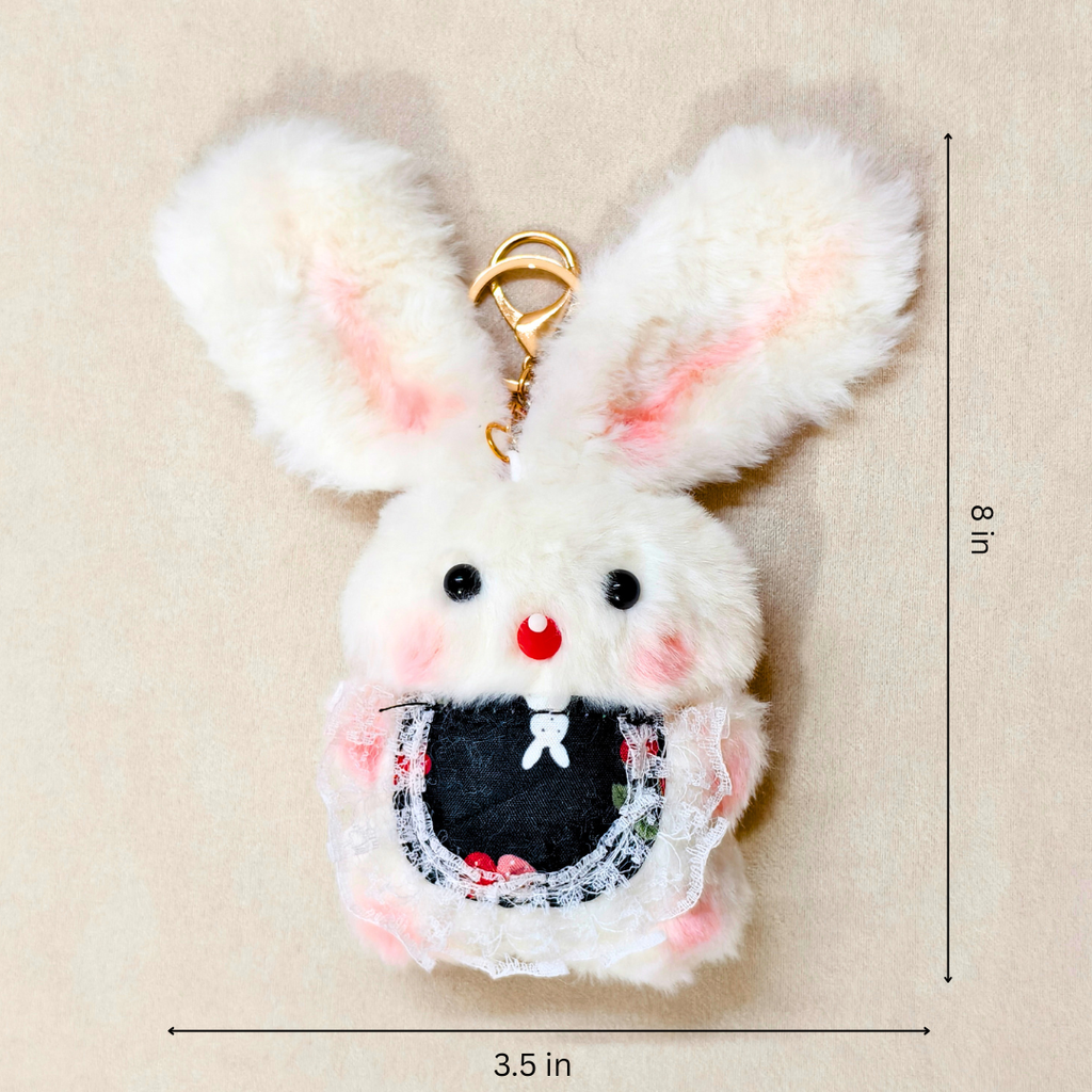 A fluffy white bunny keychain charm with pink-tipped ears, a gold clasp, and a black embroidered bib detail, shown on a beige background with dimension lines indicating 8 in height and 3.5 in width.