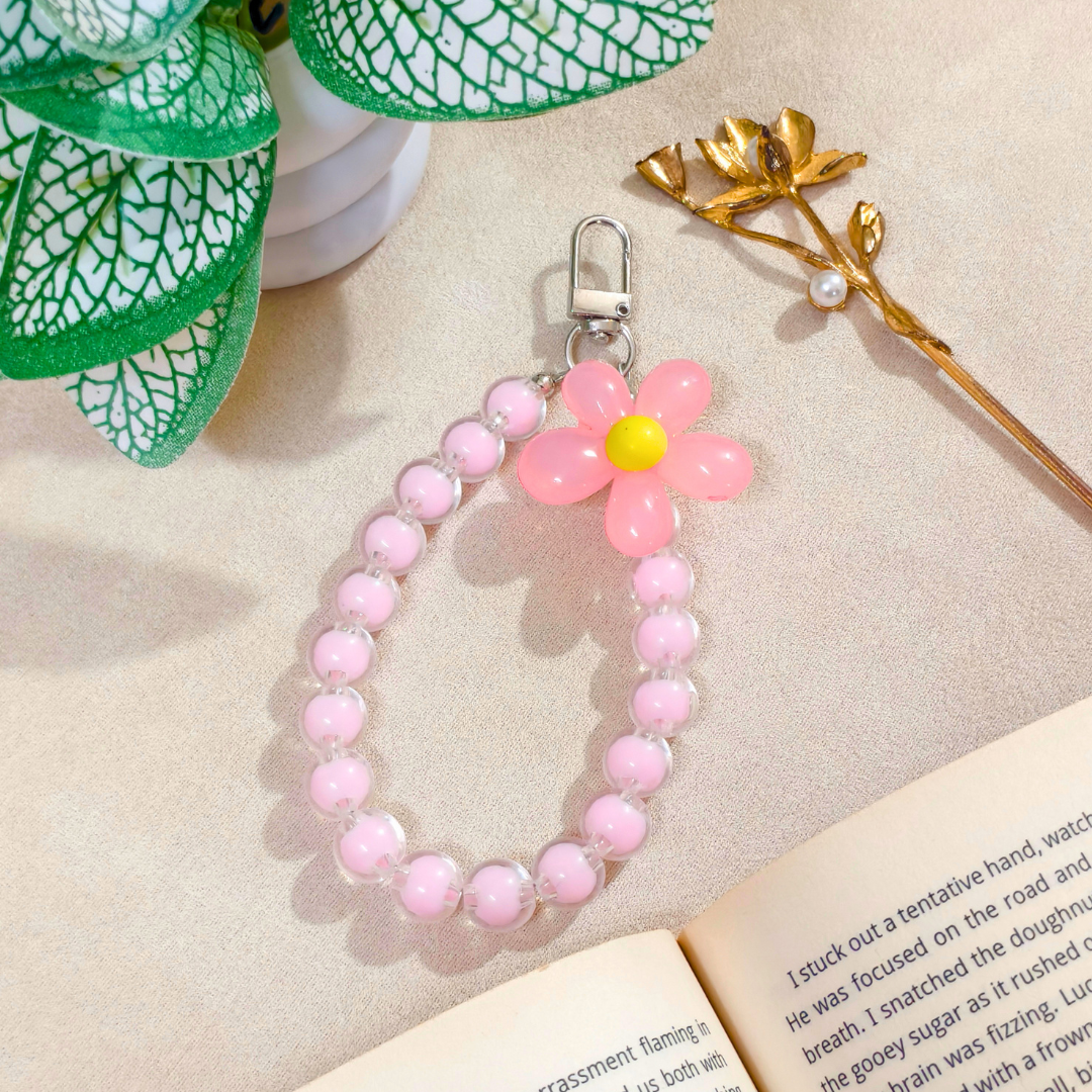 Pink beaded keychain with a flower charm on a beige surface with a book and plant.