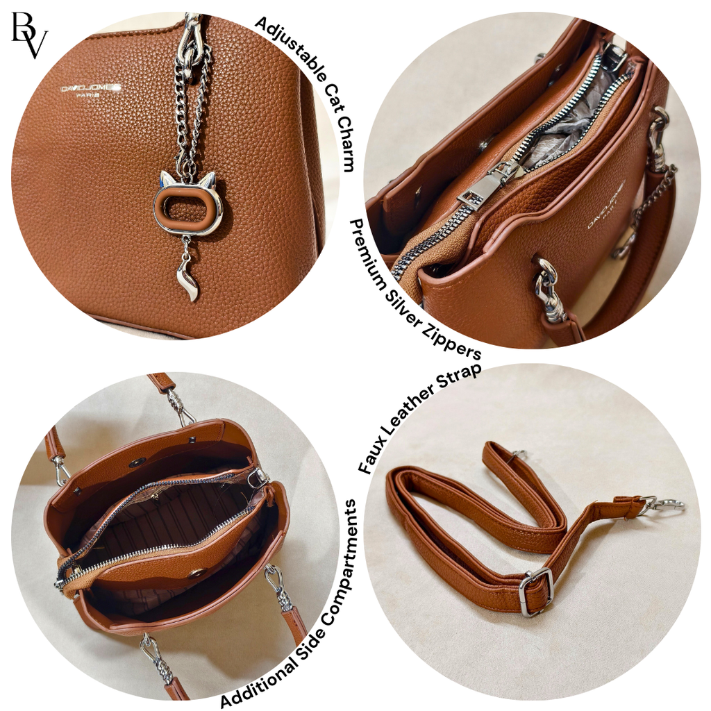 Brown leather handbag with cat charm, silver zippers, and faux leather strap on a white background.