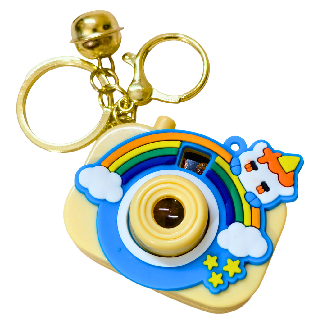 A novelty retro instant camera keychain with a gold-tone bell and split ring, featuring a colorful rainbow, white clouds, yellow stars, and a cartoon character on a light yellow body.