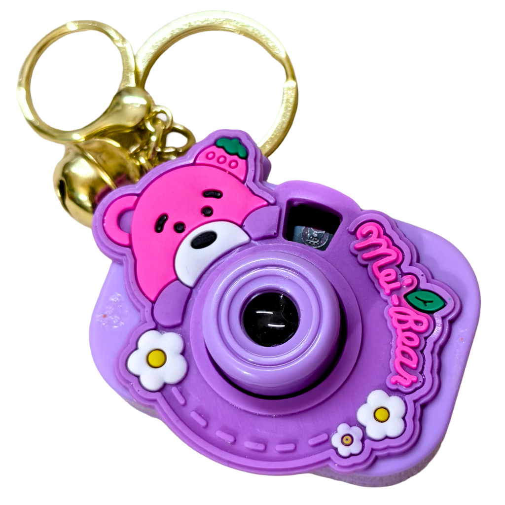 A purple cartoon camera keychain featuring a pink bear face, white flowers, and a gold split keyring on a plain white background.