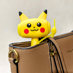 A yellow Pikachu-themed zip tie with a dangling yellow loop is shown clipped onto a brown textured handbag against a light beige background.