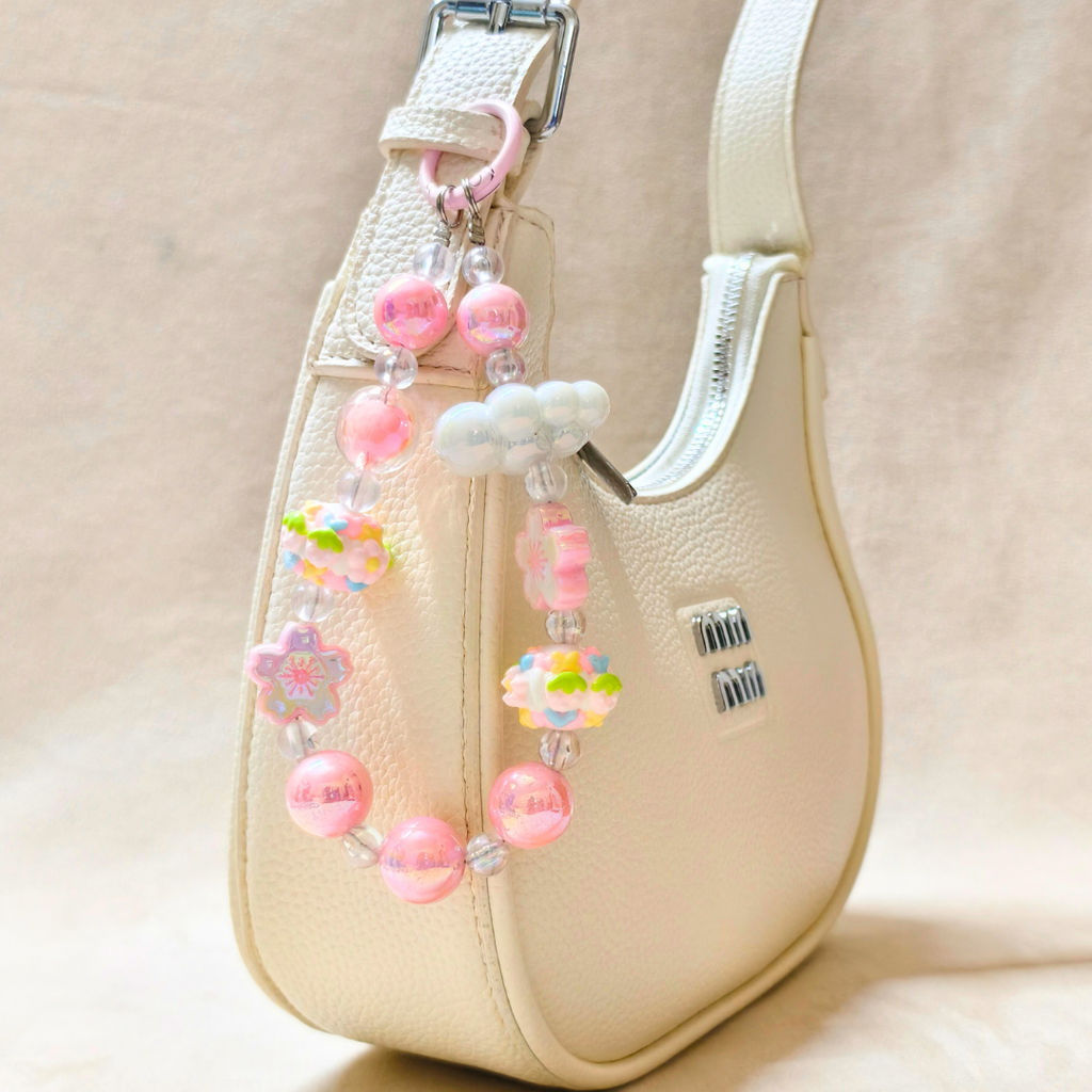 Beige handbag with a decorative strap featuring pink beads, flowers, and a cloud charm.