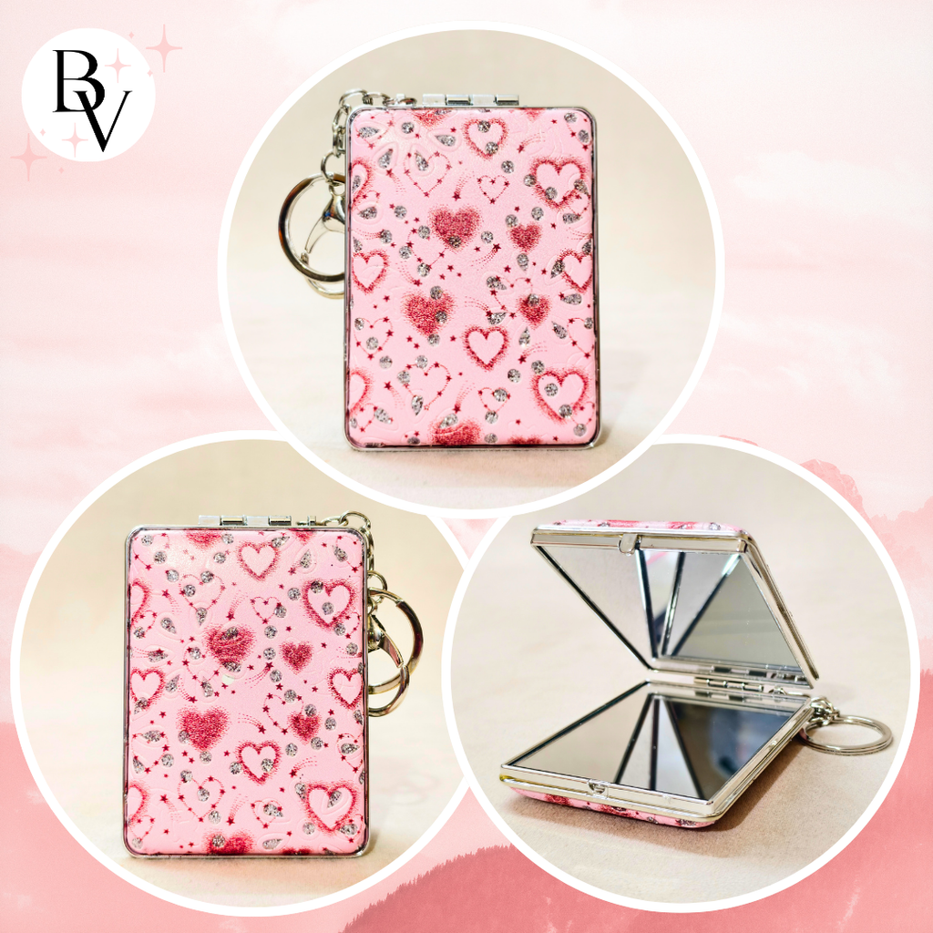 Pink compact mirror keychain with a heart pattern, shown closed and open to reveal a mirror, set against a soft pink background with circular frames and a BV logo in the top left.