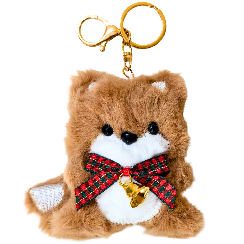A brown plush dog keychain with a white chest, black eyes and nose, a red and green plaid ribbon bow, and a small gold bell, attached to a gold metal key ring and clasp on a white background.
