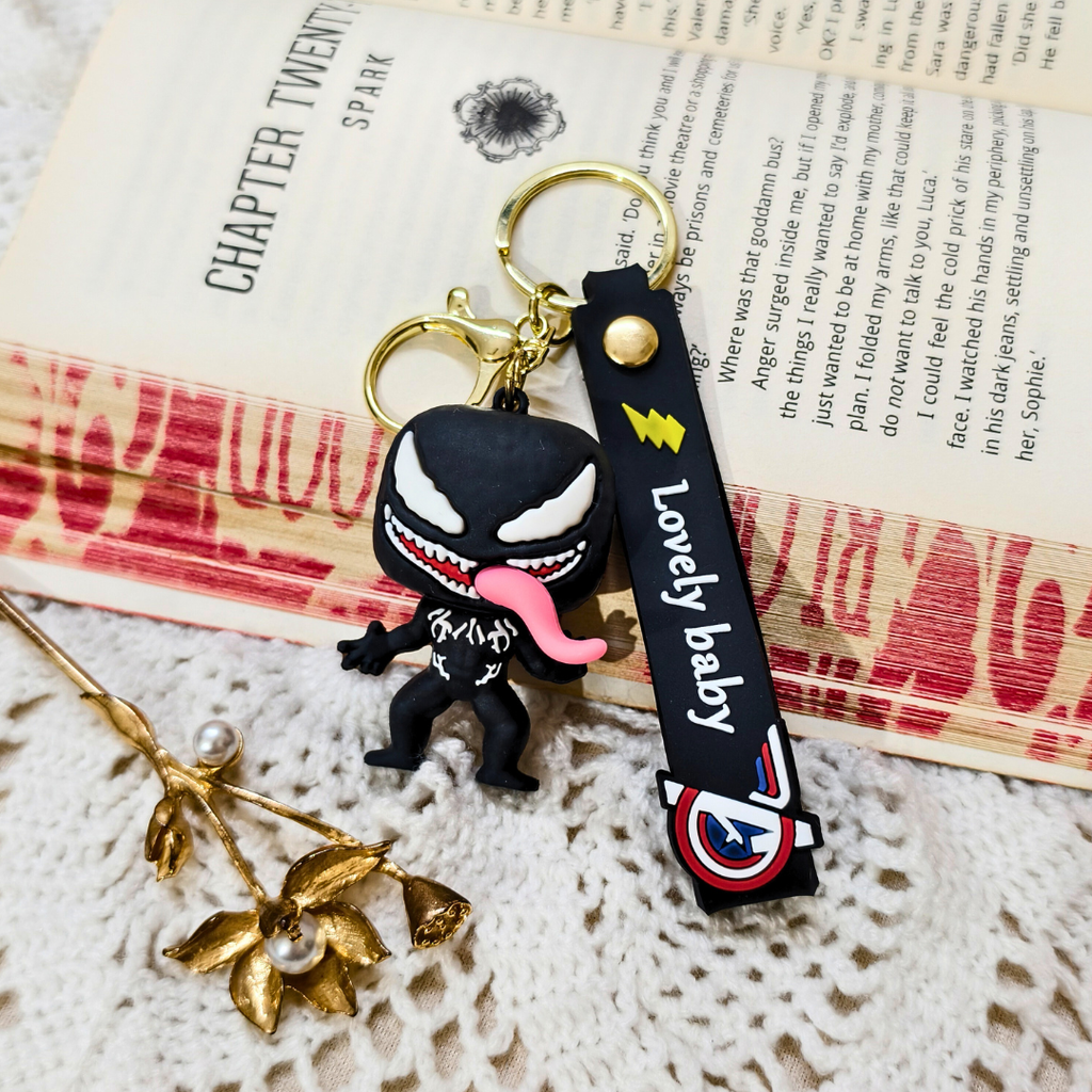 Venom character keychain placed on a open book page, beside a gold bun stick.