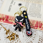 Venom character keychain placed on a open book page, beside a gold bun stick.