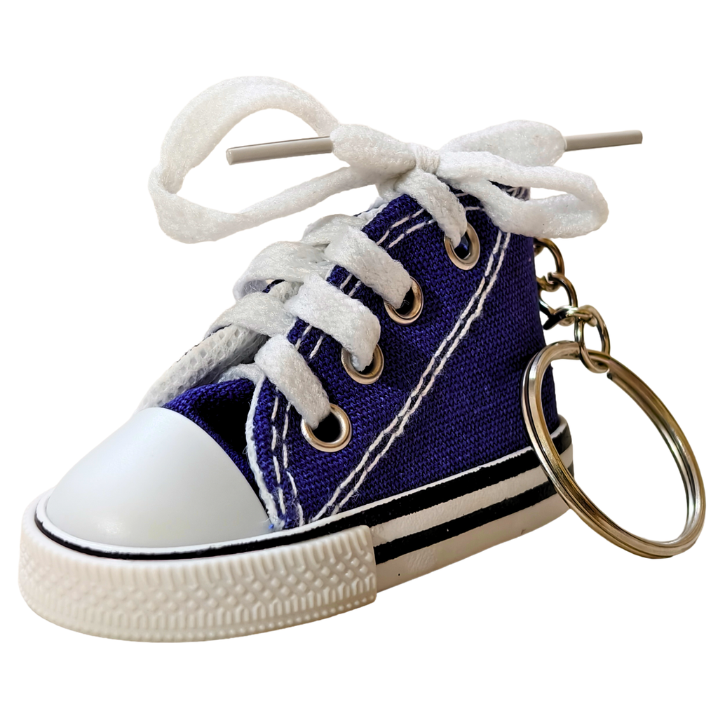 A miniature high-top canvas sneaker keychain in purple and white, featuring a white rubber toe cap, white laces tied with a wooden stick, and a gold metal key ring.