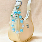 Decorative keychain with blue beads and a butterfly charm on a beige handbag.