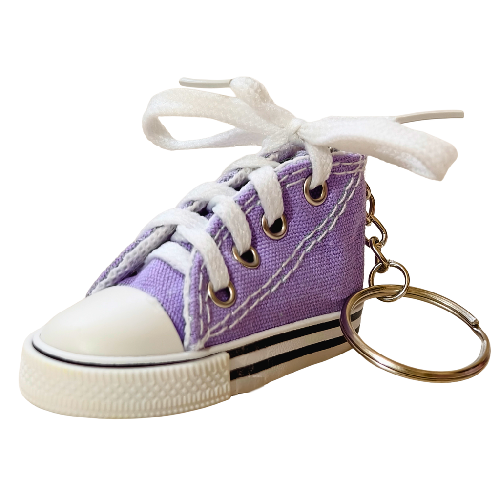 A miniature purple canvas high-top sneaker keychain with white laces tied in a bow, a white rubber toe cap, and a gold-tone key ring on a plain white background.