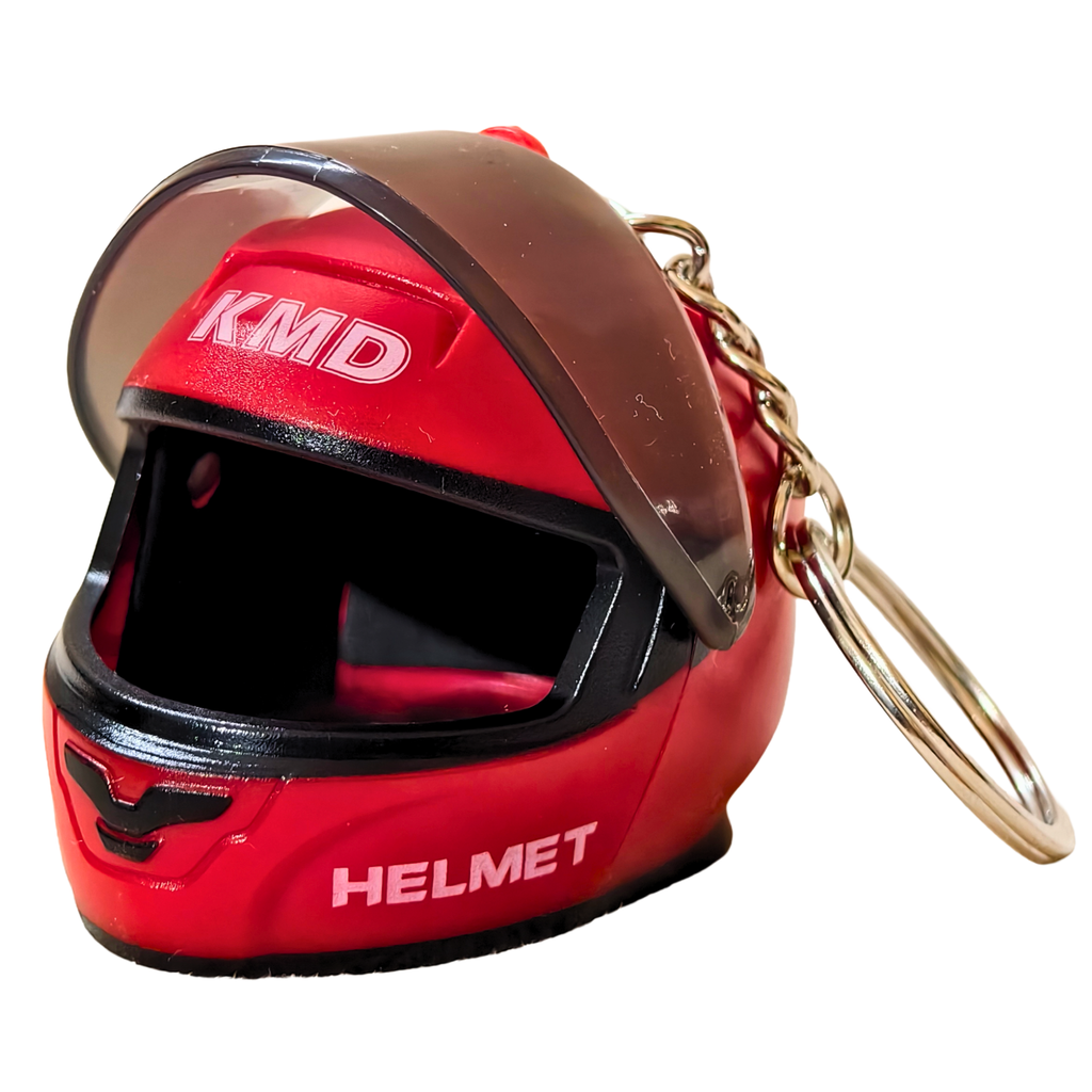 A miniature red helmet keychain with a clear visor, black trim, white 'KMD' and 'HELMET' text, and a gold-tone metal key ring on a white background.