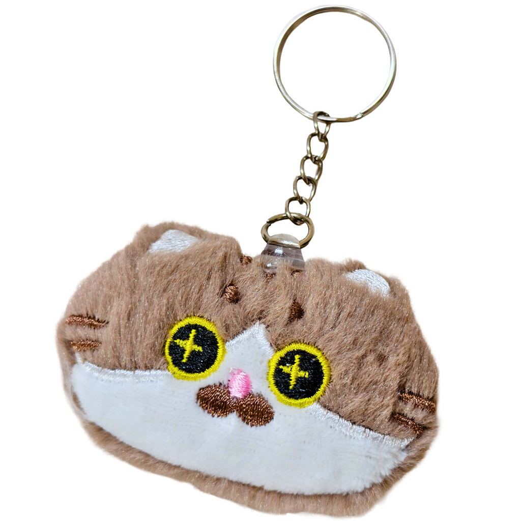 A plush keychain shaped like a small brown and white cat face, held in a person's hand. The keychain has yellow embroidered eyes with black pupils, a pink nose, and a silver metal key ring and chain on a white background.