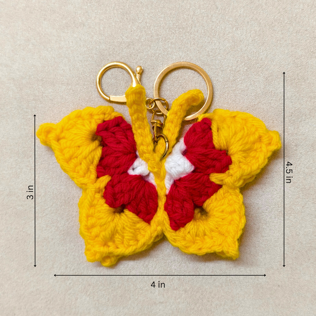 Crocheted butterfly keychain with red center and gold keyring on beige background