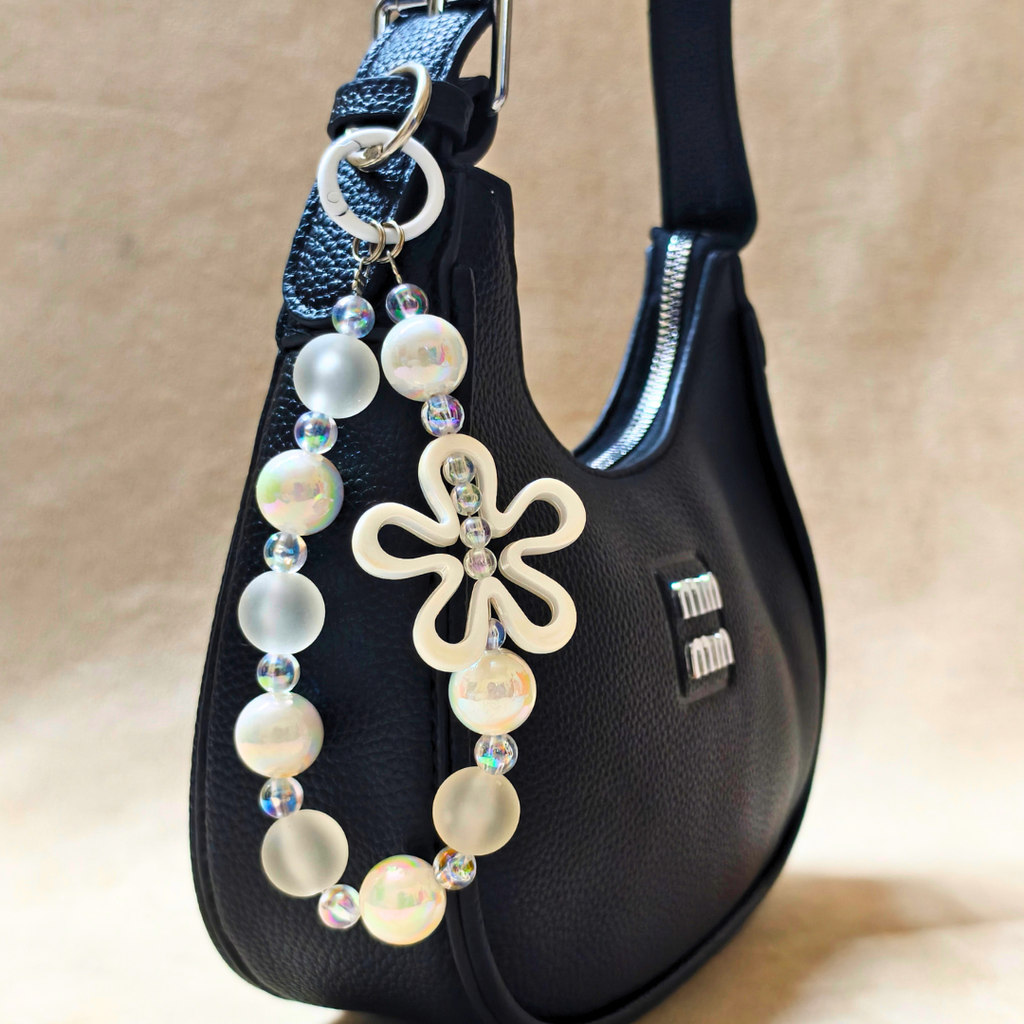 Black handbag with a decorative keychain featuring beads and a flower charm on a beige background