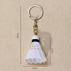 A white plastic shuttlecock keychain with a silver metal split ring and chain, shown on a beige textured background with black dimension lines and text indicating measurements of 3.5 in, 1.