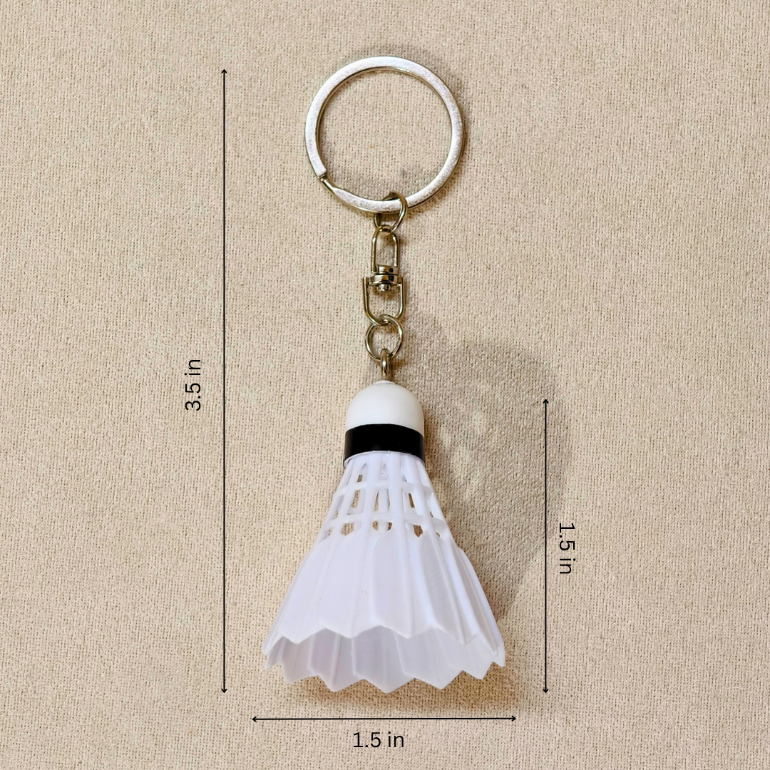 A white plastic shuttlecock keychain with a silver metal split ring and chain, shown on a beige textured background with black dimension lines and text indicating measurements of 3.5 in, 1.