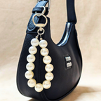 Black handbag with a pearl keychain on a beige background