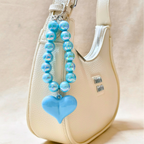 Blue beaded keychain with a heart charm attached to a beige handbag.