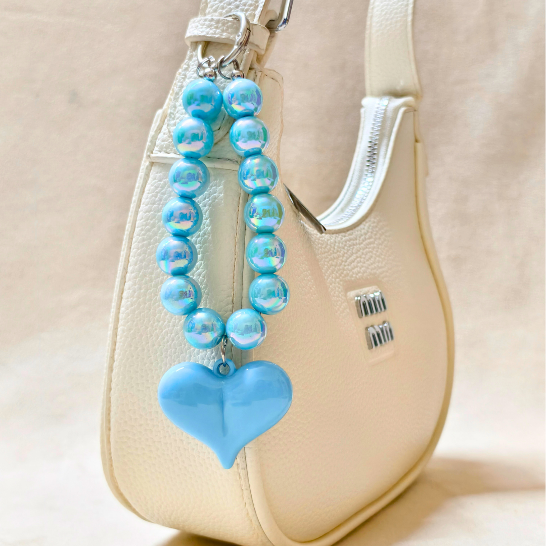 Blue beaded keychain with a heart charm attached to a beige handbag.