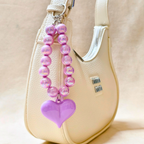 Pink beaded keychain with a heart charm attached to a beige handbag.