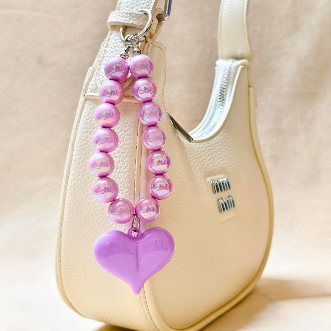Pink beaded keychain with a heart charm attached to a beige handbag.