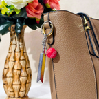 silver metal Cricket Bat and Ball  keychain with a small Cricket Ball attached, Displayed on Tan handbag as bag charm against a plain beige background.


